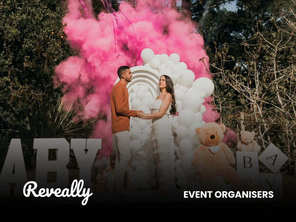 A couple at a gender reveal celebration amid pink smoke and balloons